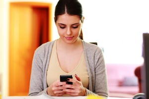 Young beautiful woman typing on smartphone at home